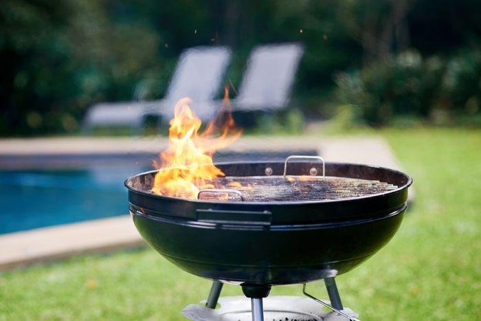 A charcoal grill in a backyard with fire flaring up through the grates.